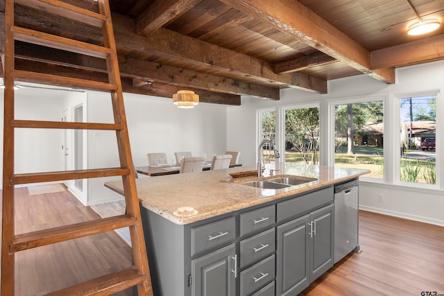 kitchen with light stone counters, a kitchen island with sink, a sink, light wood-style floors, and stainless steel dishwasher