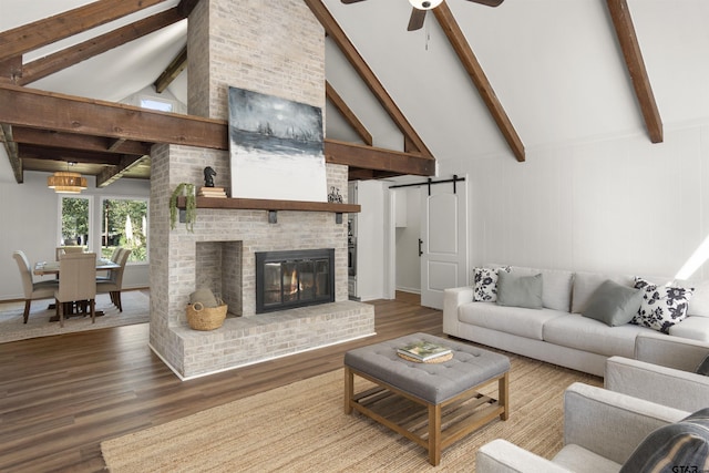 living room featuring beam ceiling, a fireplace, a barn door, ceiling fan, and wood finished floors