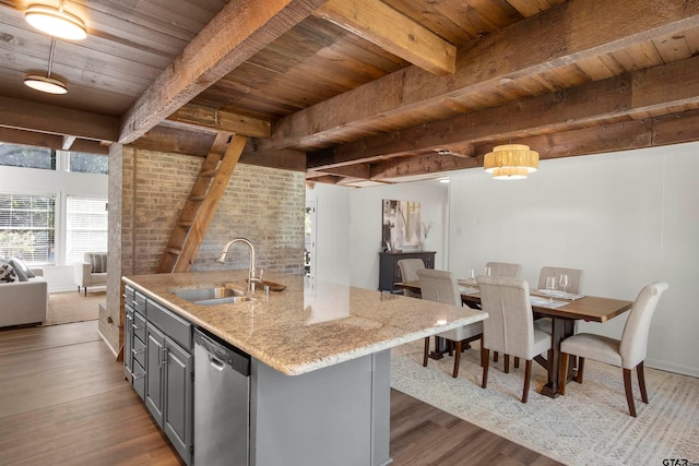 kitchen featuring light stone counters, a kitchen island with sink, a sink, gray cabinets, and dishwasher