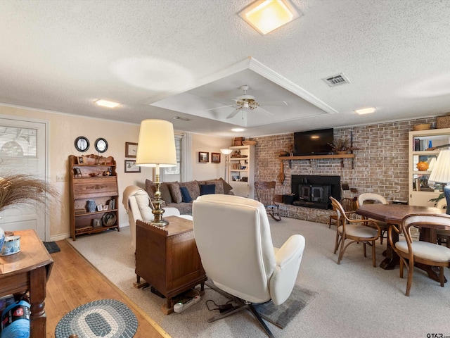 living room with a tray ceiling, ceiling fan, brick wall, and a textured ceiling