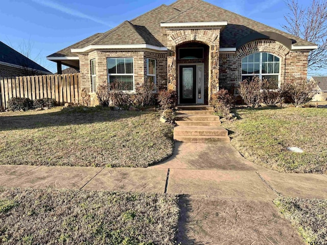 view of front of home featuring a front yard, brick siding, fence, and roof with shingles