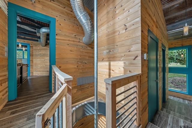 corridor with wooden walls, dark wood-style floors, and an upstairs landing