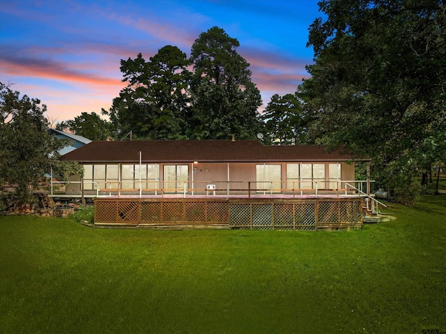 back house at dusk featuring a sunroom and a yard