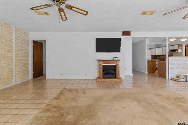 unfurnished living room with ceiling fan, light tile patterned flooring, a textured ceiling, and brick wall