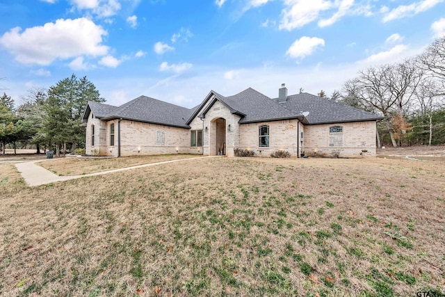 french country inspired facade featuring brick siding, a chimney, a front lawn, and roof with shingles