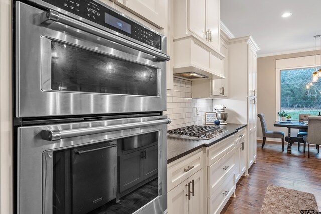 kitchen with stainless steel appliances, ornamental molding, dark countertops, and white cabinetry