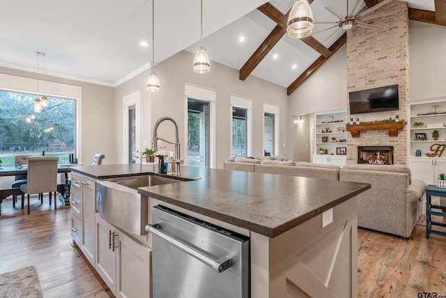 kitchen featuring white cabinets, open floor plan, dishwasher, an island with sink, and dark countertops