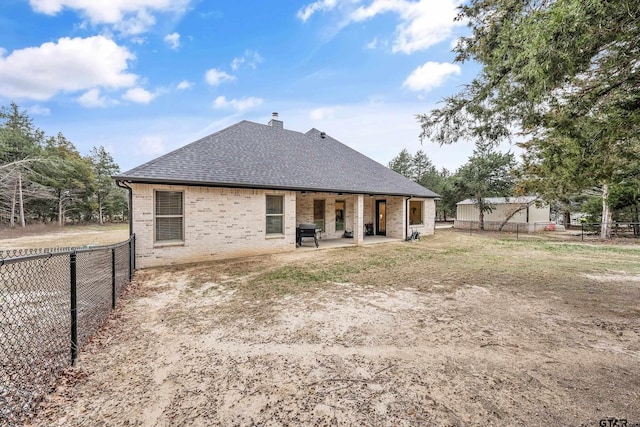 rear view of property featuring roof with shingles, brick siding, a chimney, a patio area, and fence