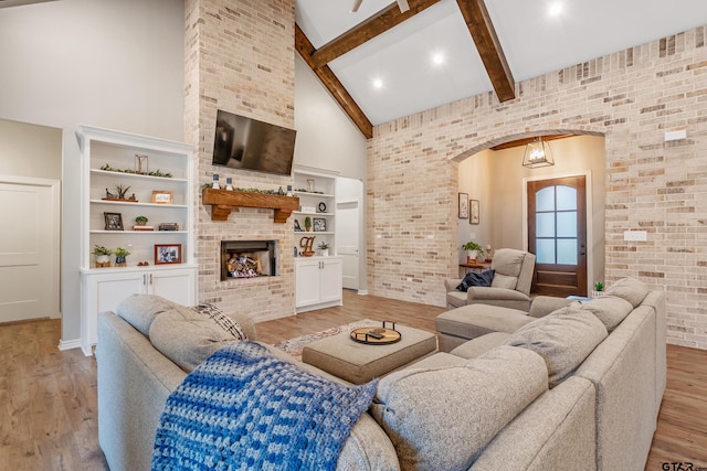 living room featuring arched walkways, beamed ceiling, light wood-type flooring, a fireplace, and high vaulted ceiling