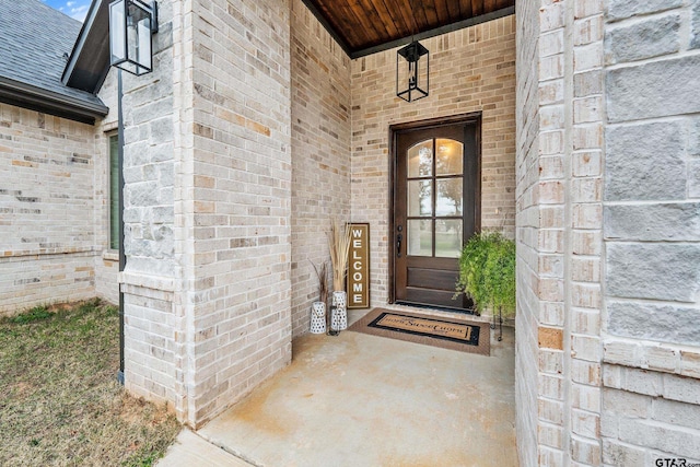 doorway to property featuring a shingled roof and brick siding