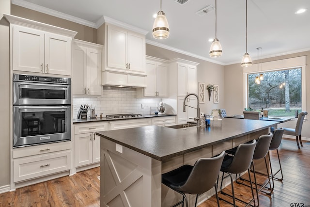 kitchen featuring an island with sink, dark countertops, a sink, and white cabinets