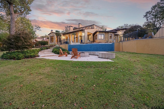 back house at dusk featuring a patio and a lawn