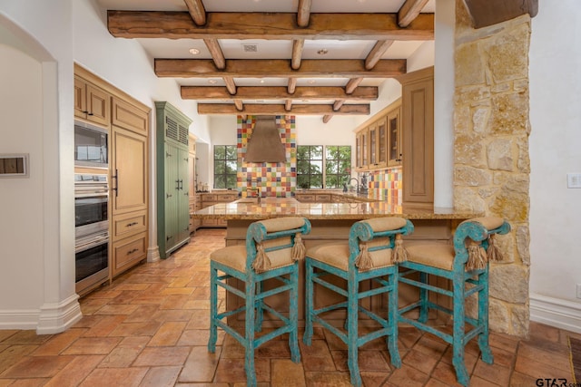 kitchen featuring kitchen peninsula, a kitchen bar, built in microwave, wall chimney range hood, and beam ceiling