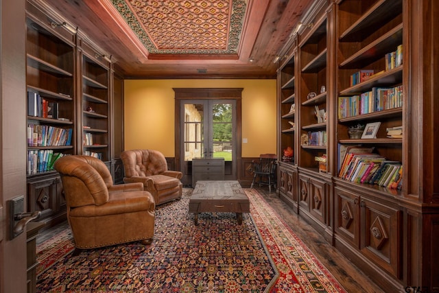 living area with built in shelves, a raised ceiling, wooden ceiling, and crown molding