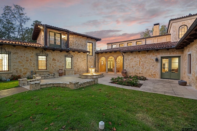 back house at dusk with french doors, a yard, a balcony, and a patio