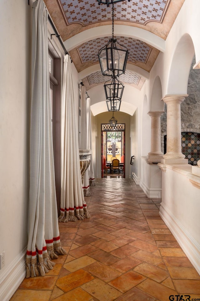 corridor featuring ornate columns, a chandelier, and lofted ceiling