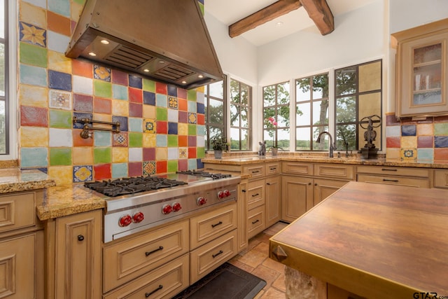 kitchen featuring beam ceiling, light stone countertops, stainless steel gas stovetop, decorative backsplash, and exhaust hood