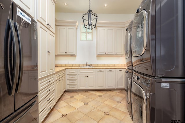 kitchen with sink, stacked washer / dryer, stainless steel fridge, a chandelier, and pendant lighting