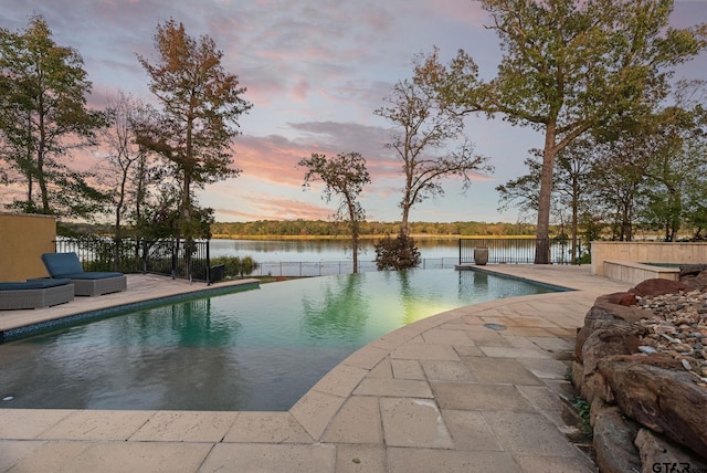 pool at dusk featuring a water view and a patio