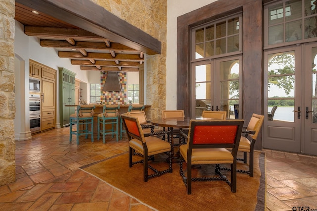 dining space with beamed ceiling, a high ceiling, and french doors