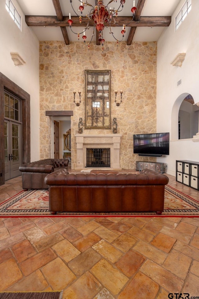 unfurnished living room featuring beamed ceiling, a towering ceiling, a fireplace, and a notable chandelier