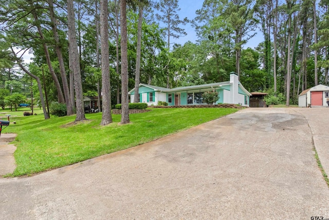 view of front of property featuring driveway, a chimney, an outdoor structure, and a front yard
