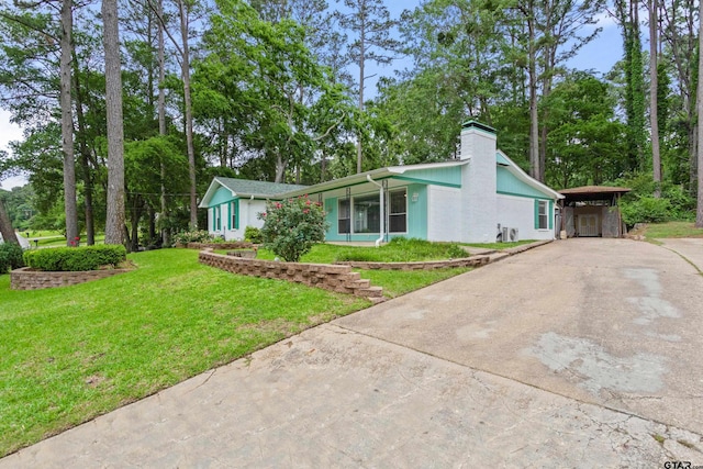 view of front of house featuring concrete driveway, a carport, a chimney, and a front lawn