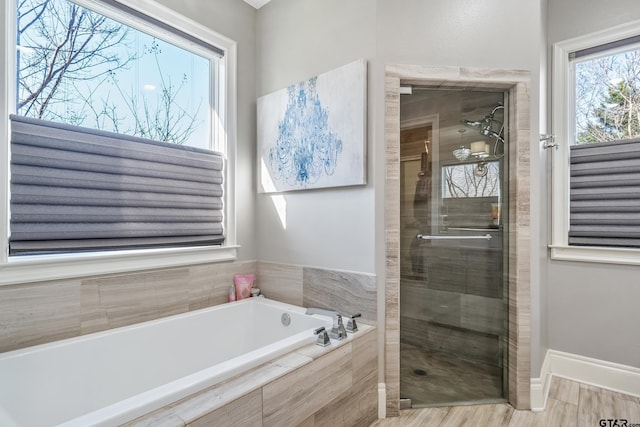 full bathroom with a stall shower, wood finished floors, a bath, and baseboards