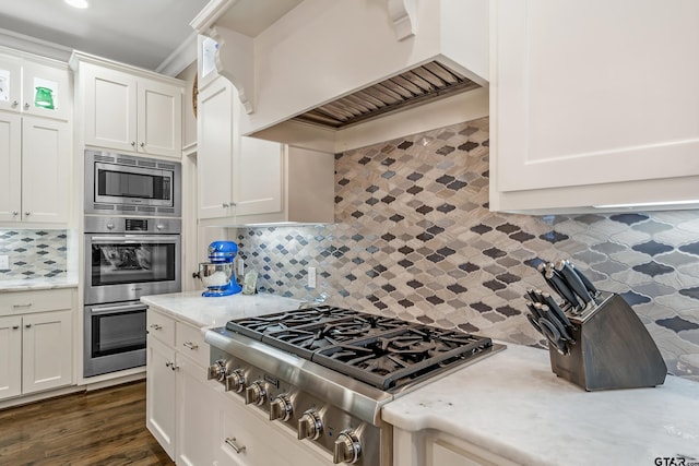 kitchen featuring custom range hood, decorative backsplash, appliances with stainless steel finishes, white cabinets, and light stone countertops