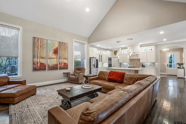 living room with high vaulted ceiling, arched walkways, dark wood-style flooring, and baseboards