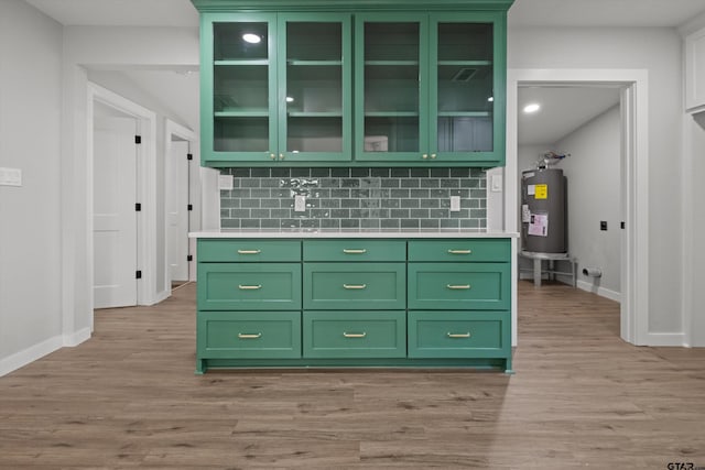 kitchen featuring decorative backsplash, green cabinets, light wood-type flooring, and water heater