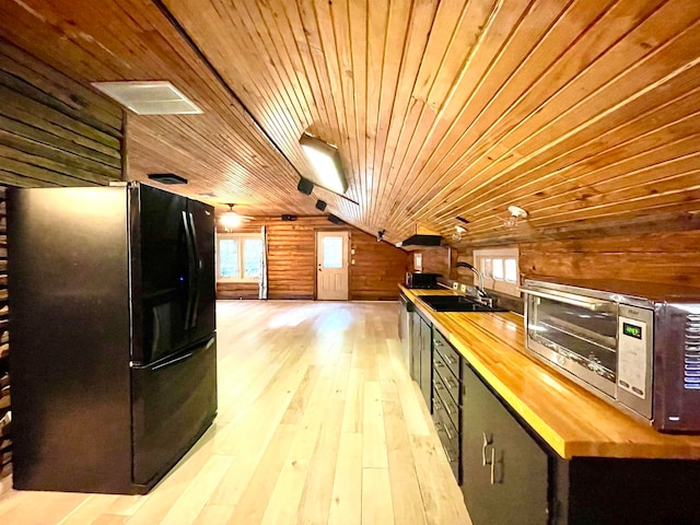 kitchen featuring sink, light hardwood / wood-style flooring, wooden walls, black fridge, and wood counters