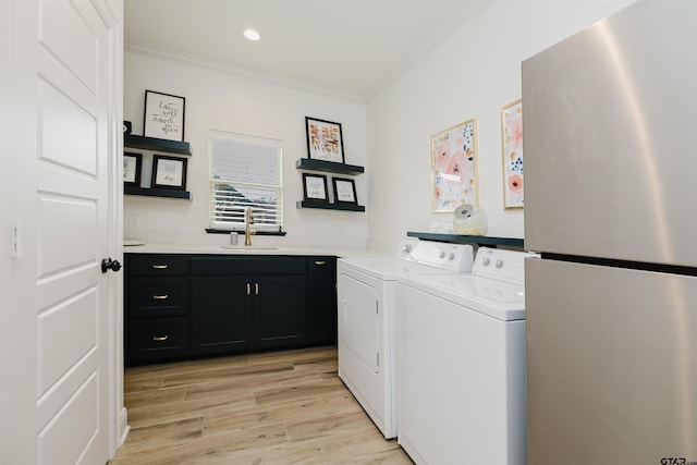 laundry area with light wood-type flooring, ornamental molding, a sink, cabinet space, and separate washer and dryer