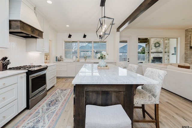 kitchen with custom exhaust hood, stainless steel range with gas stovetop, plenty of natural light, and light stone countertops