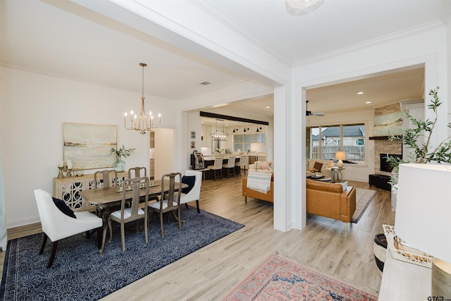 dining space with visible vents, ornamental molding, ceiling fan with notable chandelier, a fireplace, and wood finished floors