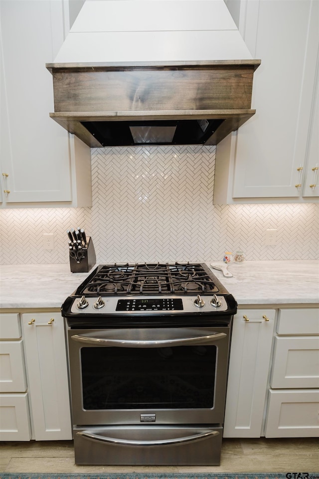 kitchen with decorative backsplash, ventilation hood, stainless steel range with gas cooktop, and light countertops