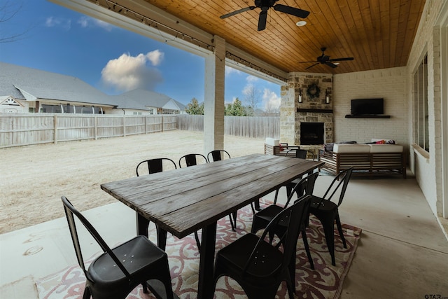 view of patio / terrace with a ceiling fan, outdoor dining area, a fenced backyard, and an outdoor stone fireplace