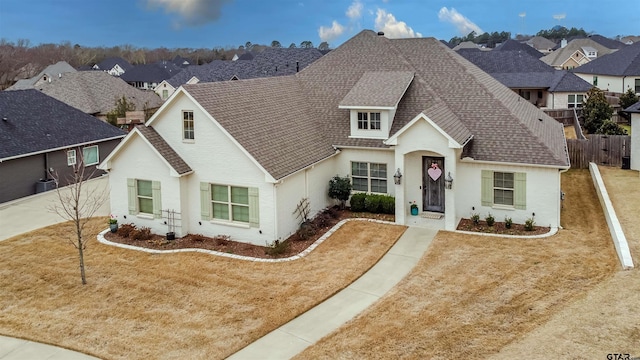 view of front of property featuring a residential view, fence, brick siding, and a shingled roof