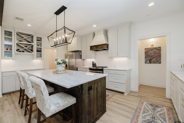 kitchen with a kitchen bar, custom range hood, a center island, light wood-style floors, and appliances with stainless steel finishes