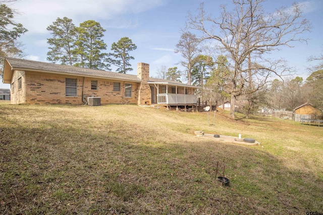 rear view of property with central AC unit and a lawn