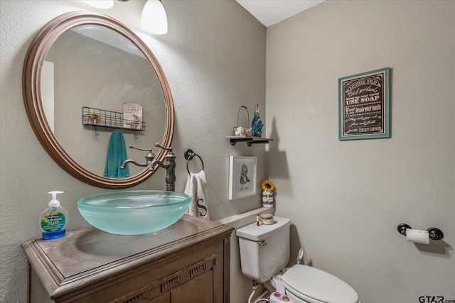 bathroom with a textured ceiling, vanity, and toilet