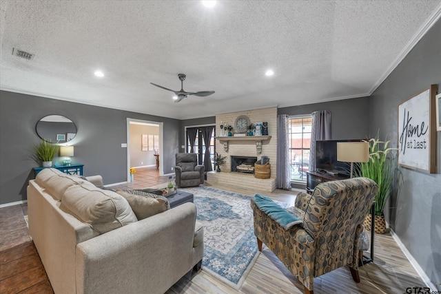 living room featuring ceiling fan, wood-type flooring, a textured ceiling, a fireplace, and ornamental molding