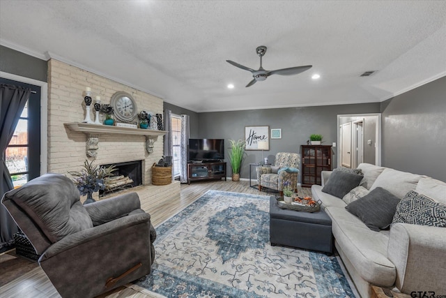 living room with ceiling fan, crown molding, hardwood / wood-style floors, a textured ceiling, and a fireplace