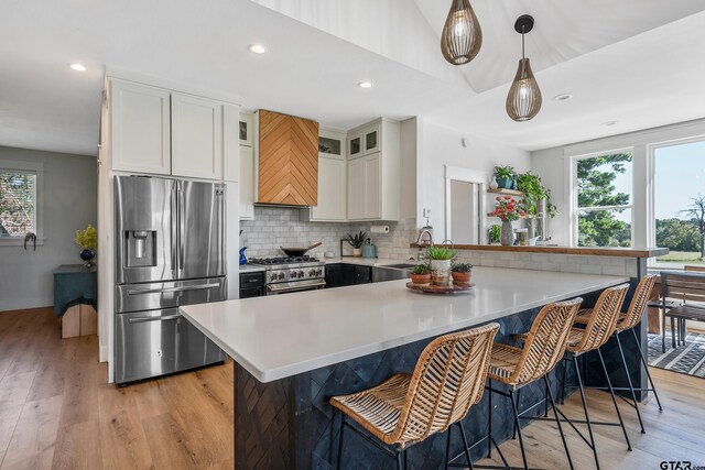 kitchen featuring light wood-type flooring, a kitchen breakfast bar, stainless steel appliances, white cabinets, and decorative backsplash