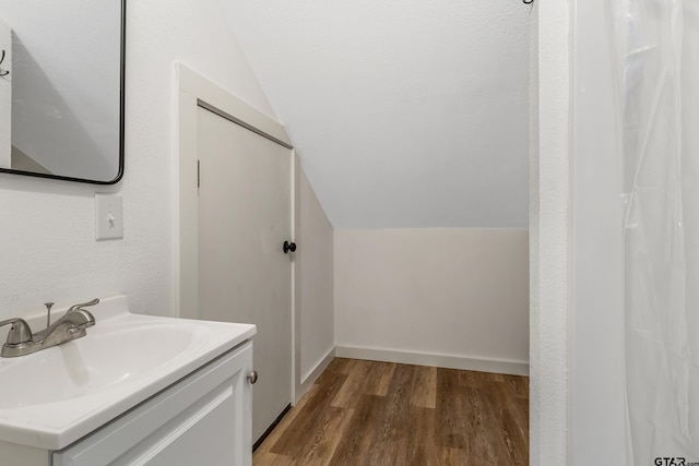 bathroom featuring baseboards, wood finished floors, vanity, and vaulted ceiling