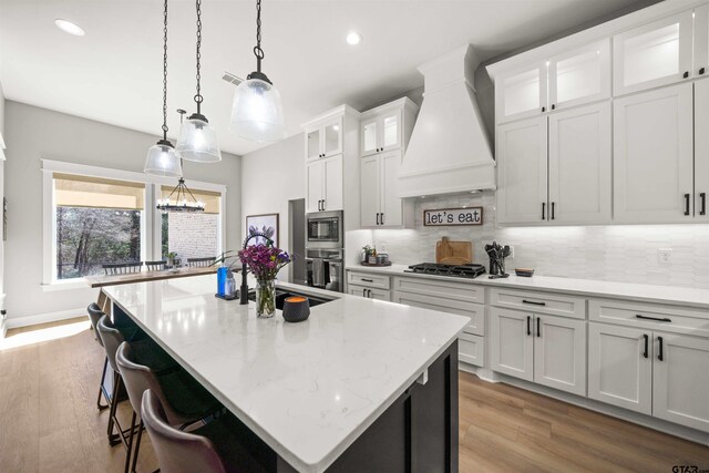 15920 Shepards Gln, Lindale, TX 75771 - kitchen featuring premium range hood, a kitchen island with sink, tasteful backsplash, stainless steel appliances, and white cabinets