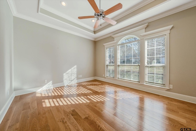 empty room with a raised ceiling, ceiling fan, ornamental molding, and light hardwood / wood-style floors