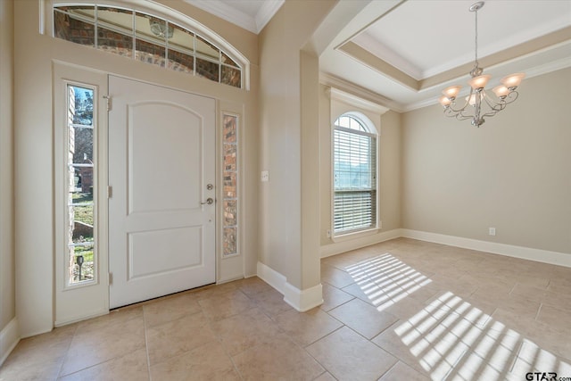 entrance foyer with a raised ceiling, light tile patterned flooring, ornamental molding, and a chandelier