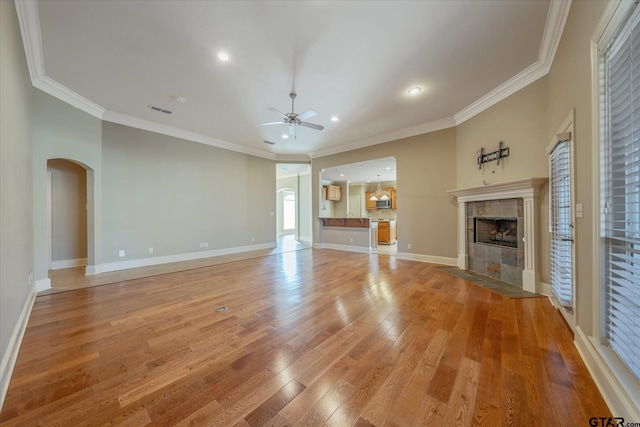 unfurnished living room featuring a tile fireplace, ornamental molding, ceiling fan, and light wood-type flooring