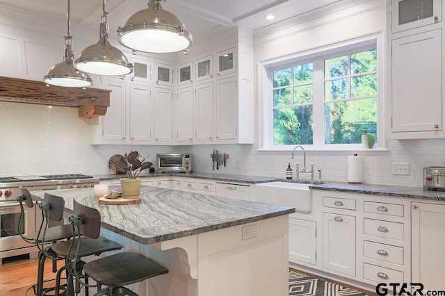 kitchen with white cabinetry, a kitchen island, hanging light fixtures, and a sink